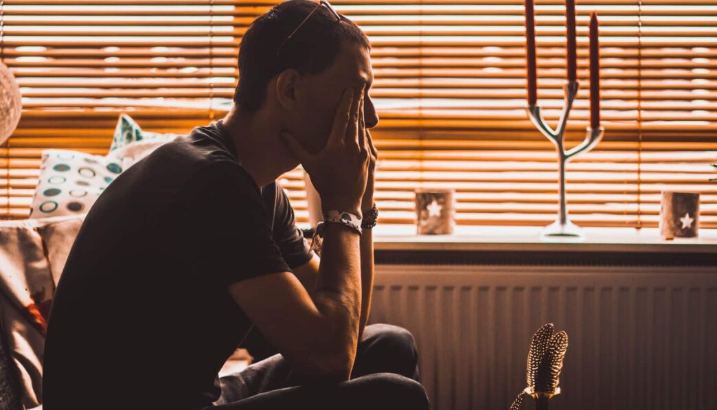 man sitting on chair covering his eyes