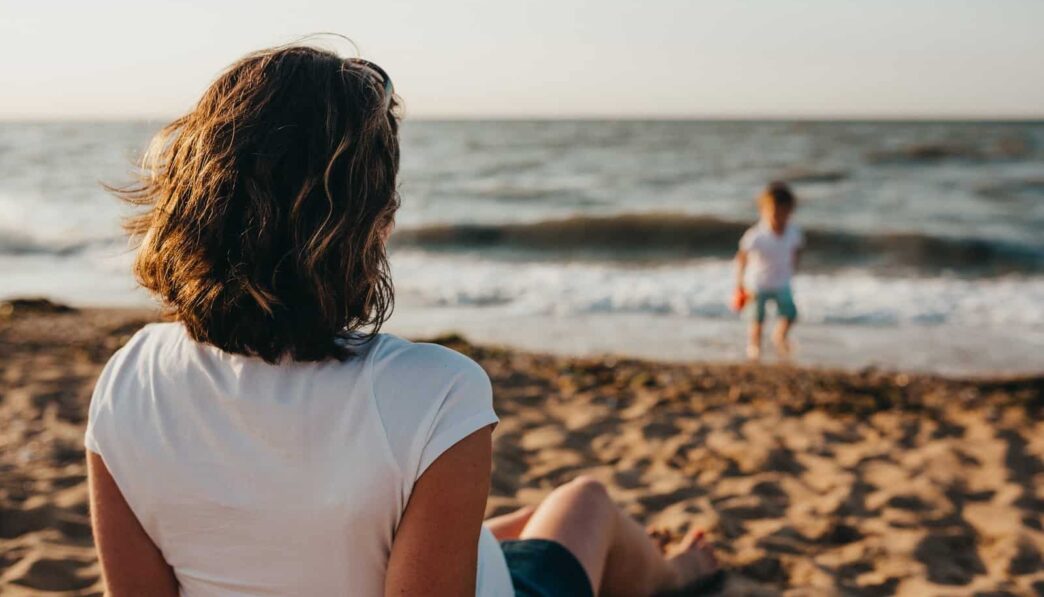 woman watching child playing on beach during daytime