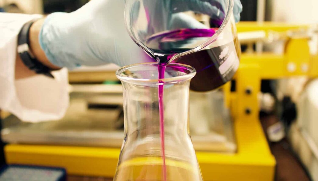 person pouring purple liquid on clear glass container
