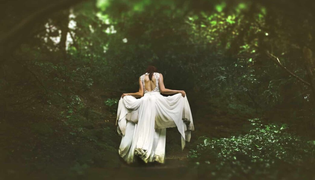 woman in white dress walking on pathway surrounded by trees