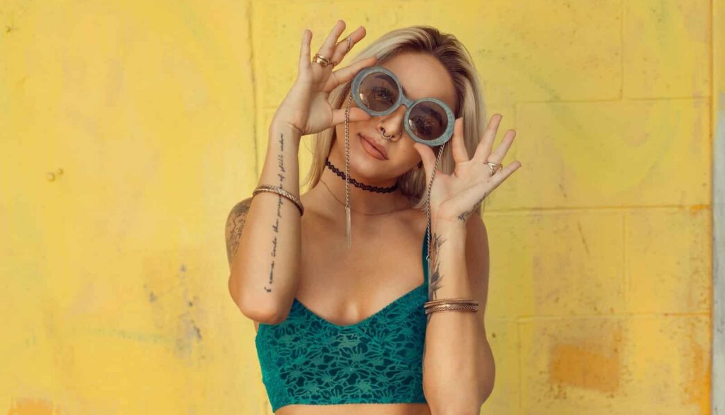 woman in blue bralette holding sunglasses putting on her eyes