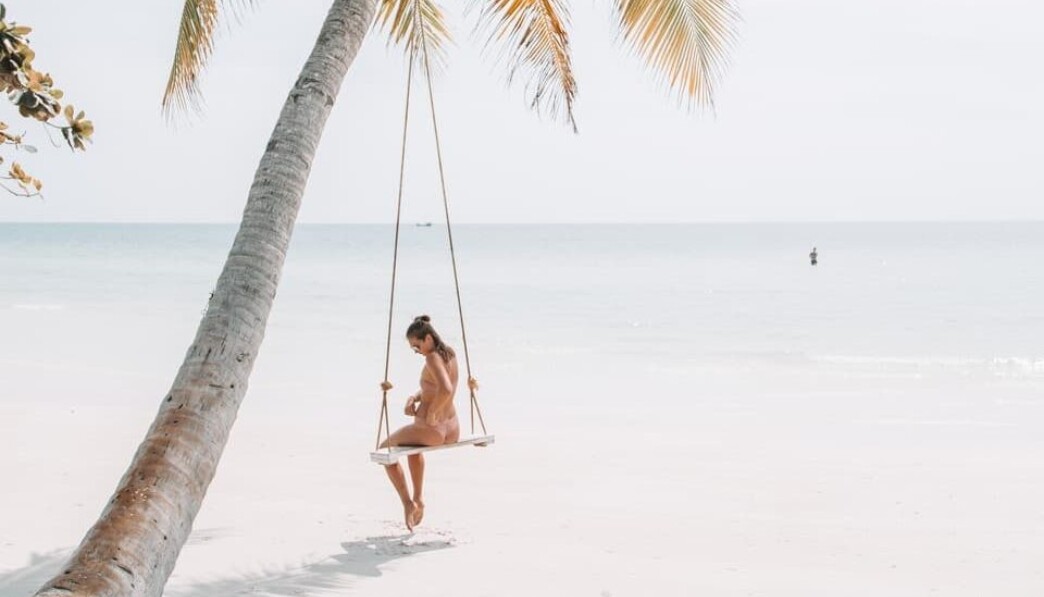 woman wearing bikini sitting on swing near coconut tree