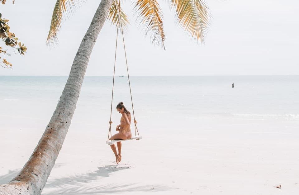 woman wearing bikini sitting on swing near coconut tree