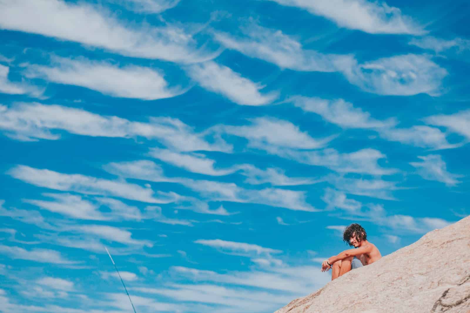 woman in black bikini sitting on rock under blue sky and white clouds during daytime