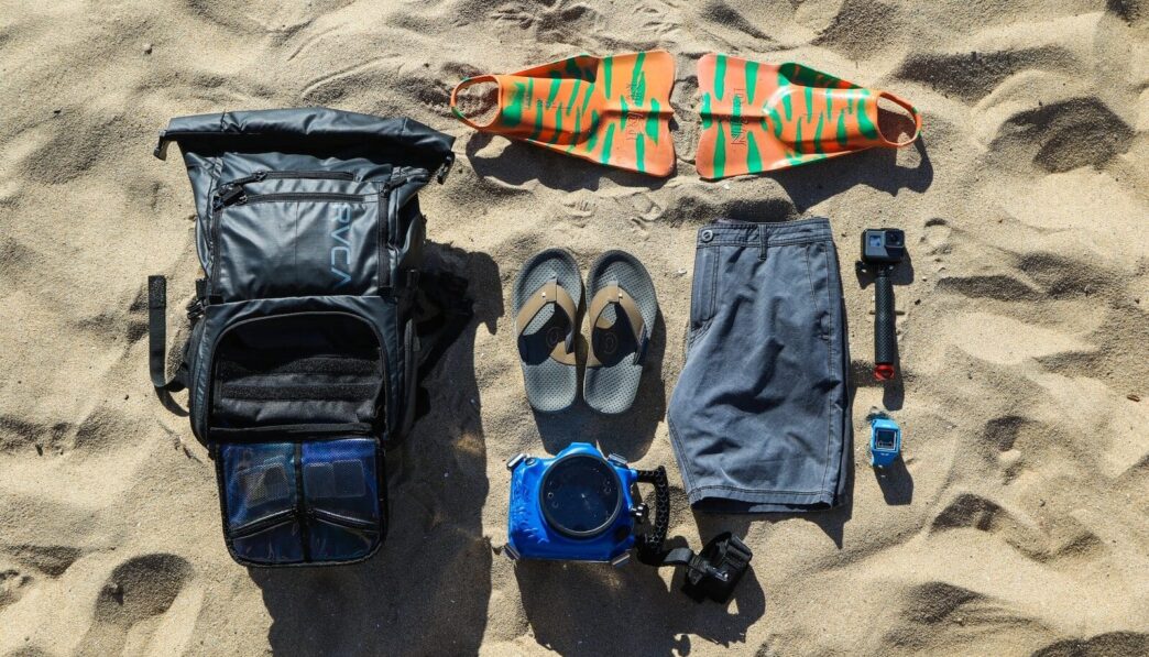 flat-lay photography of flip-flops, hiking backpack, board, shorts, and action camera