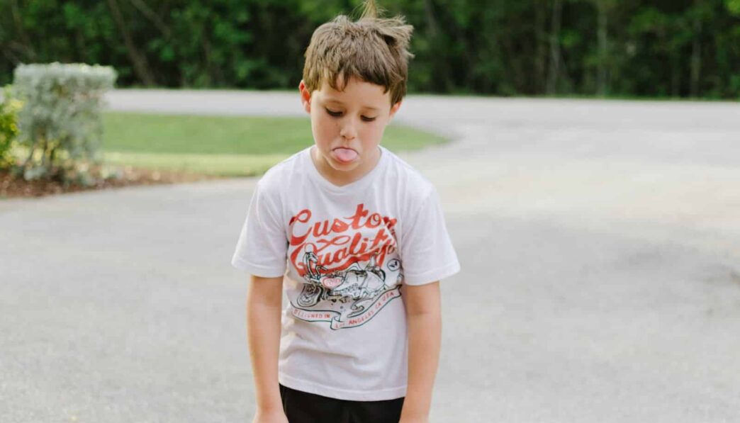 boy standing on gray concrete road while tongue out