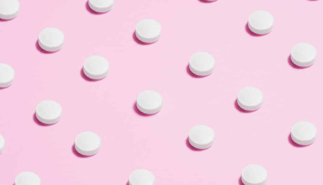 Flat lay of white pills on a pastel pink surface, showcasing a medical theme.