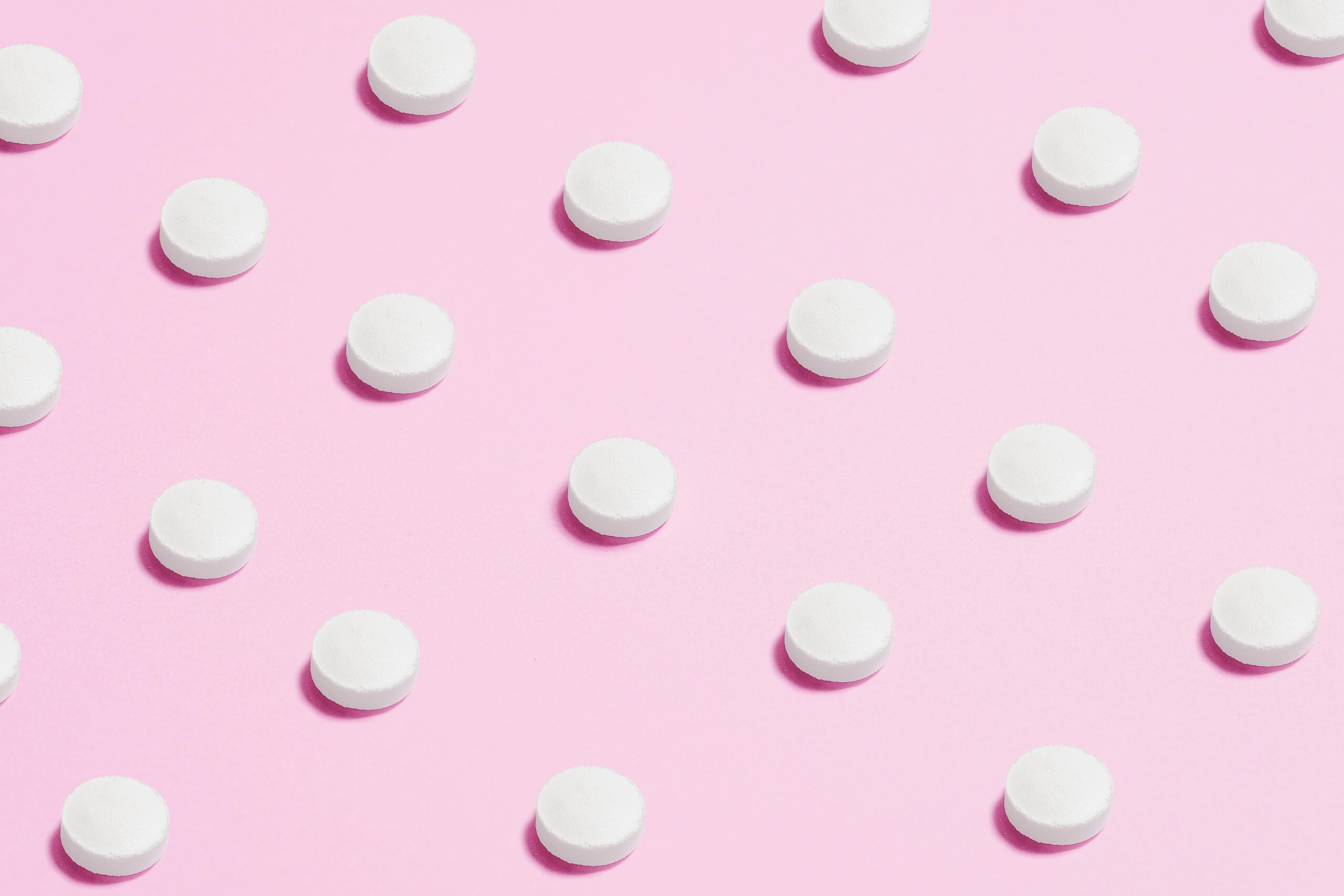 Flat lay of white pills on a pastel pink surface, showcasing a medical theme.