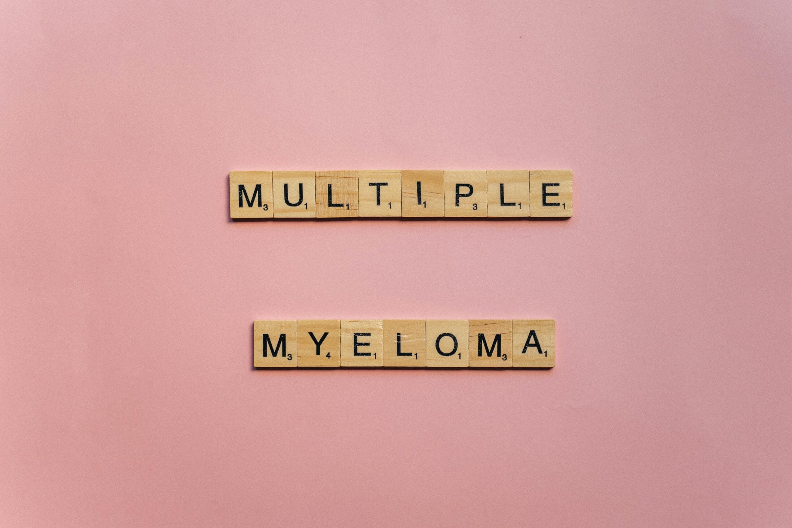 Wooden letter tiles spelling 'Multiple Myeloma' on a pink background.