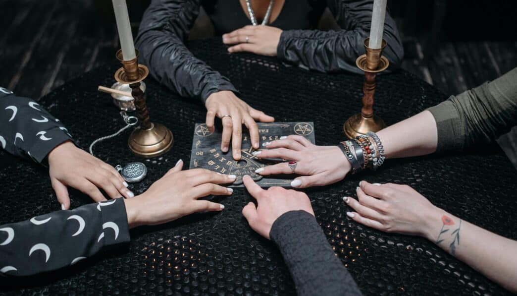 A group gathered around a Ouija board, exploring spirituality and the occult in a dimly lit room.
