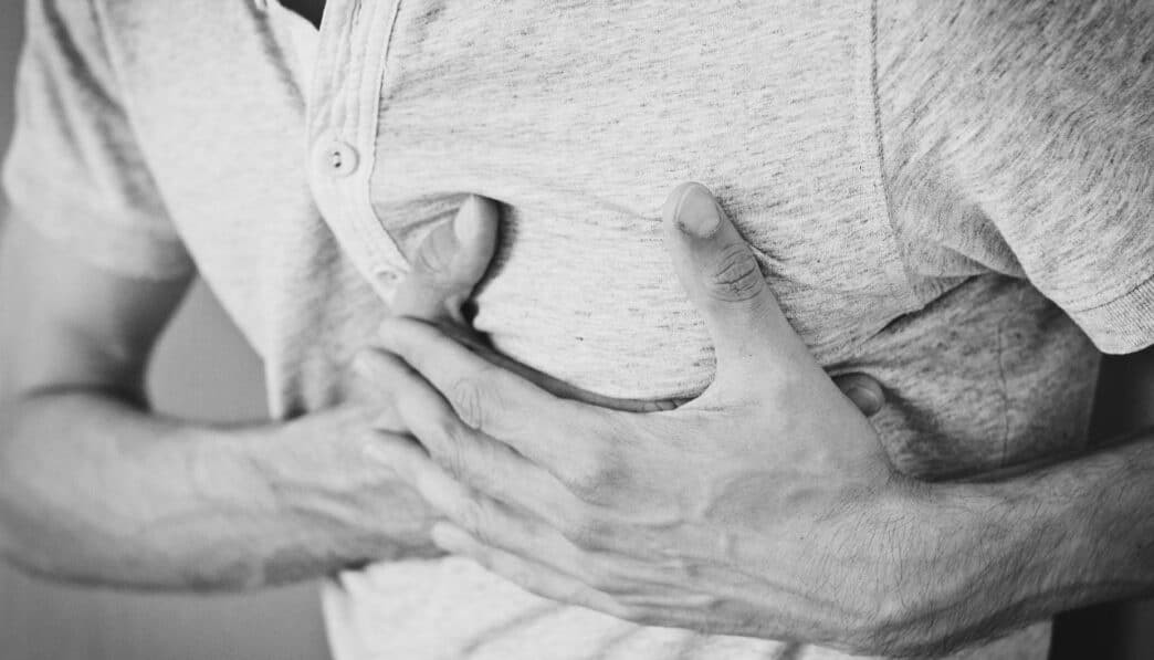 Black and white photo of a man clutching his chest, indicating discomfort or pain.